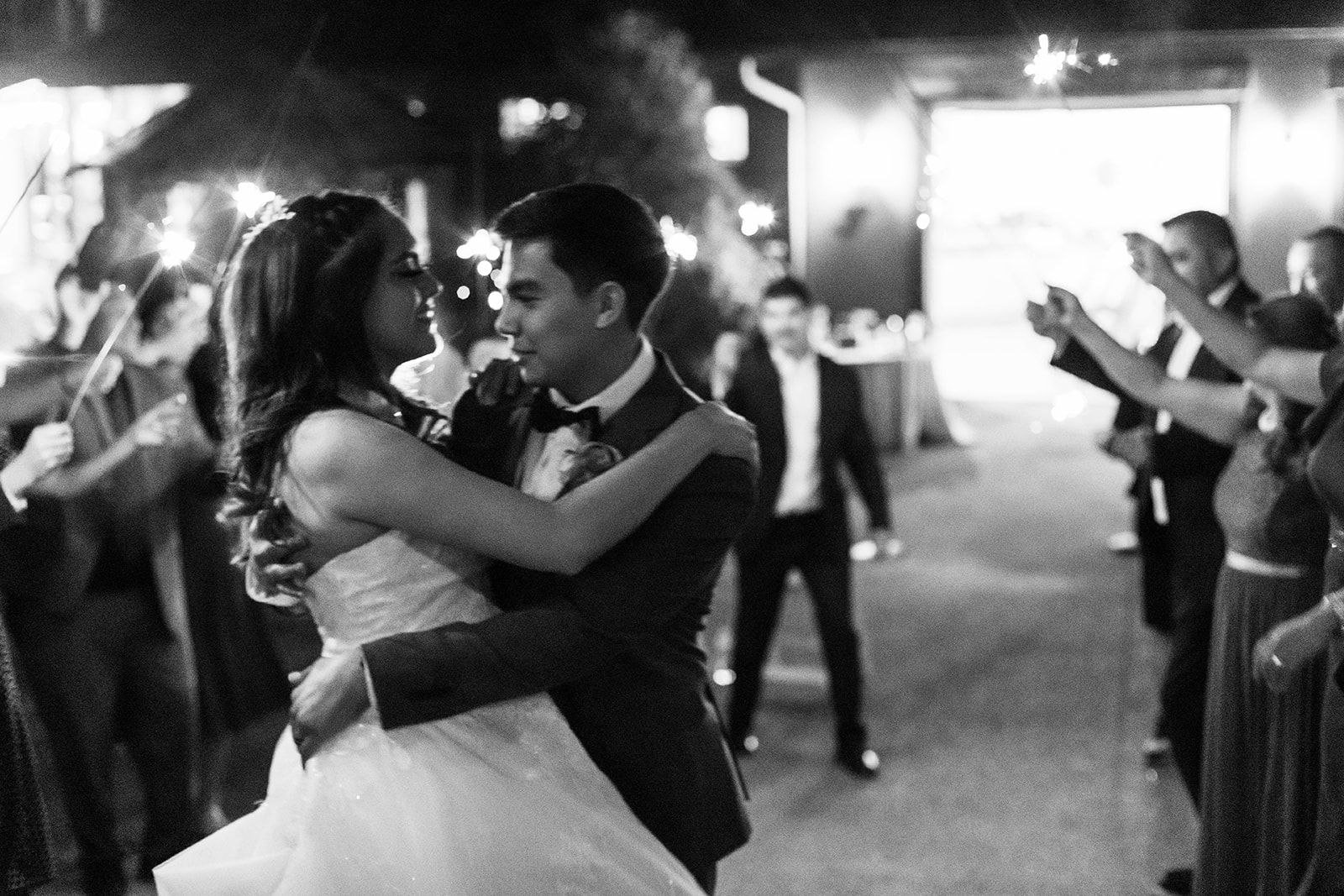 Dance Floor Embrace Black-and-white image of a couple in wedding attire embracing on a crowded dance floor.