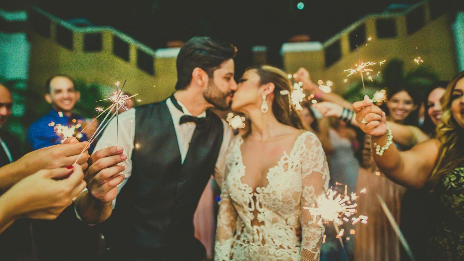 Couple in wedding attire kissing while guests hold sparklers around them.