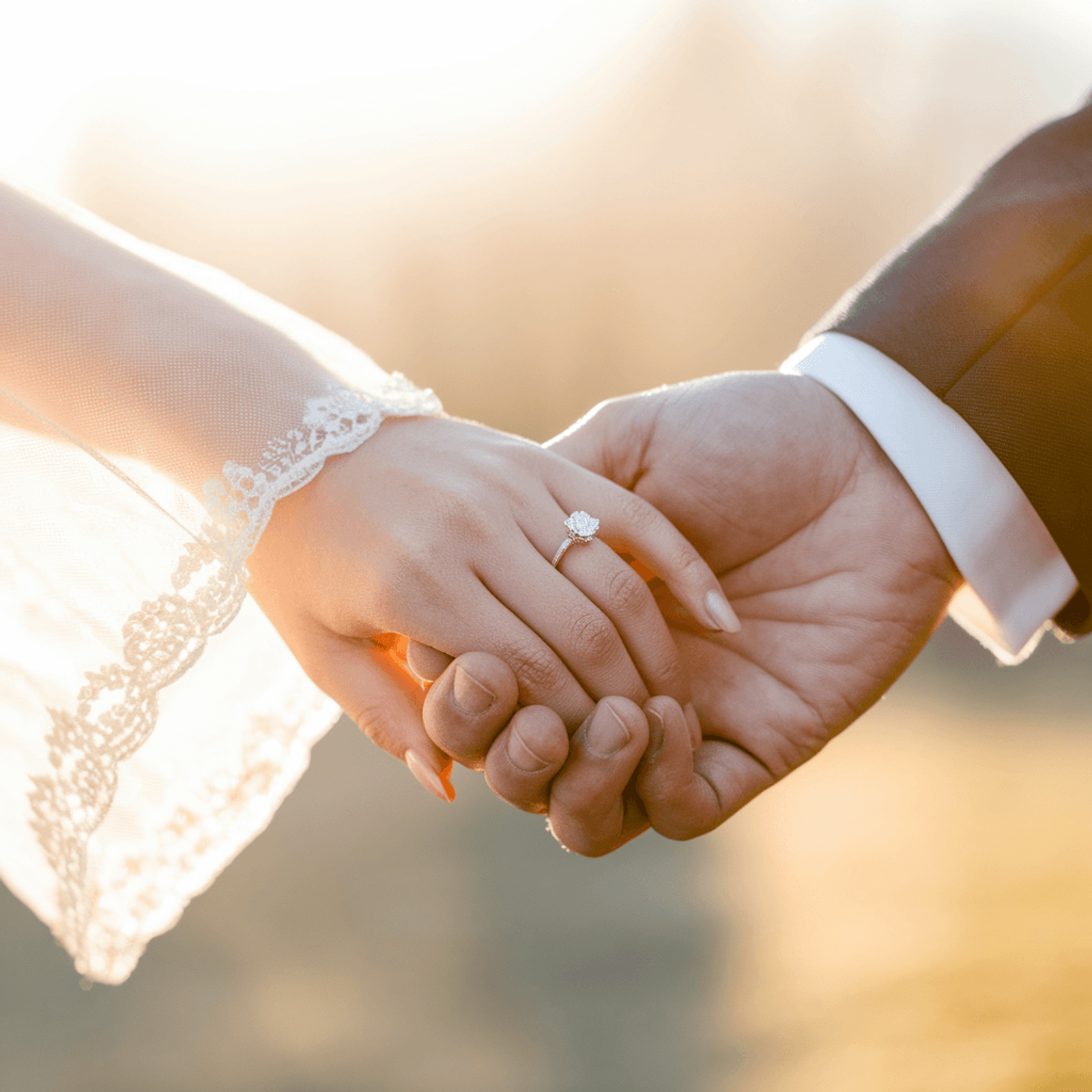 Close-up of two people in wedding attire holding hands in sunlight.