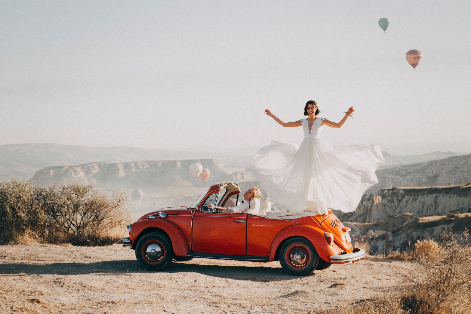 Vintage Car Portrait Person in a white dress standing on a red vintage convertible in a rocky landscape.