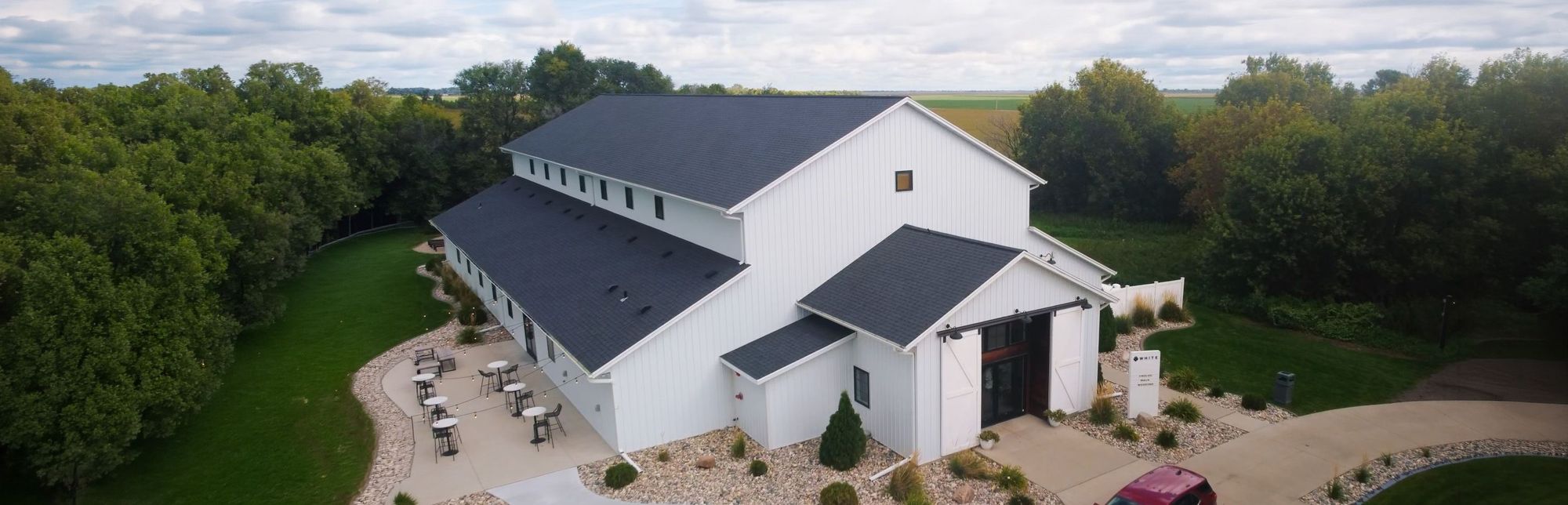 White Building Aerial Aerial view of a large white barn-like building surrounded by trees and lawn.