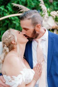 Outdoor Kiss Close-up of a couple in wedding attire kissing outdoors while one holds a white bouquet.