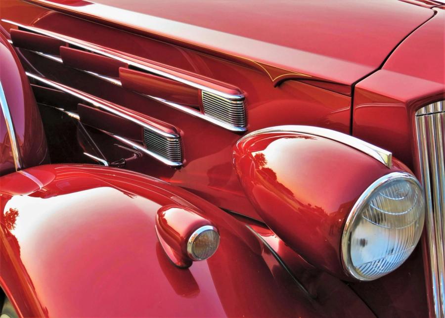 Vintage Car Detail Close-up of the chrome grille and headlight of a red vintage car.