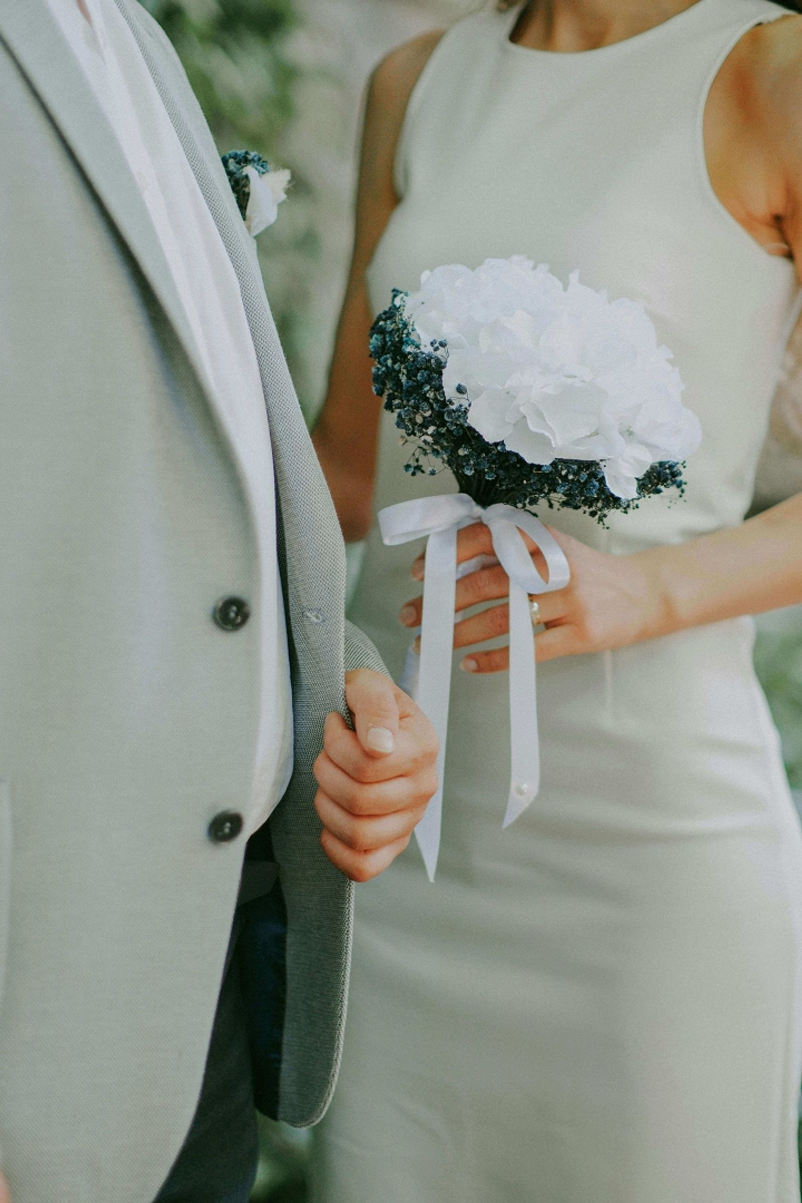 Close crop of two people in formal attire, one holding a white bouquet.