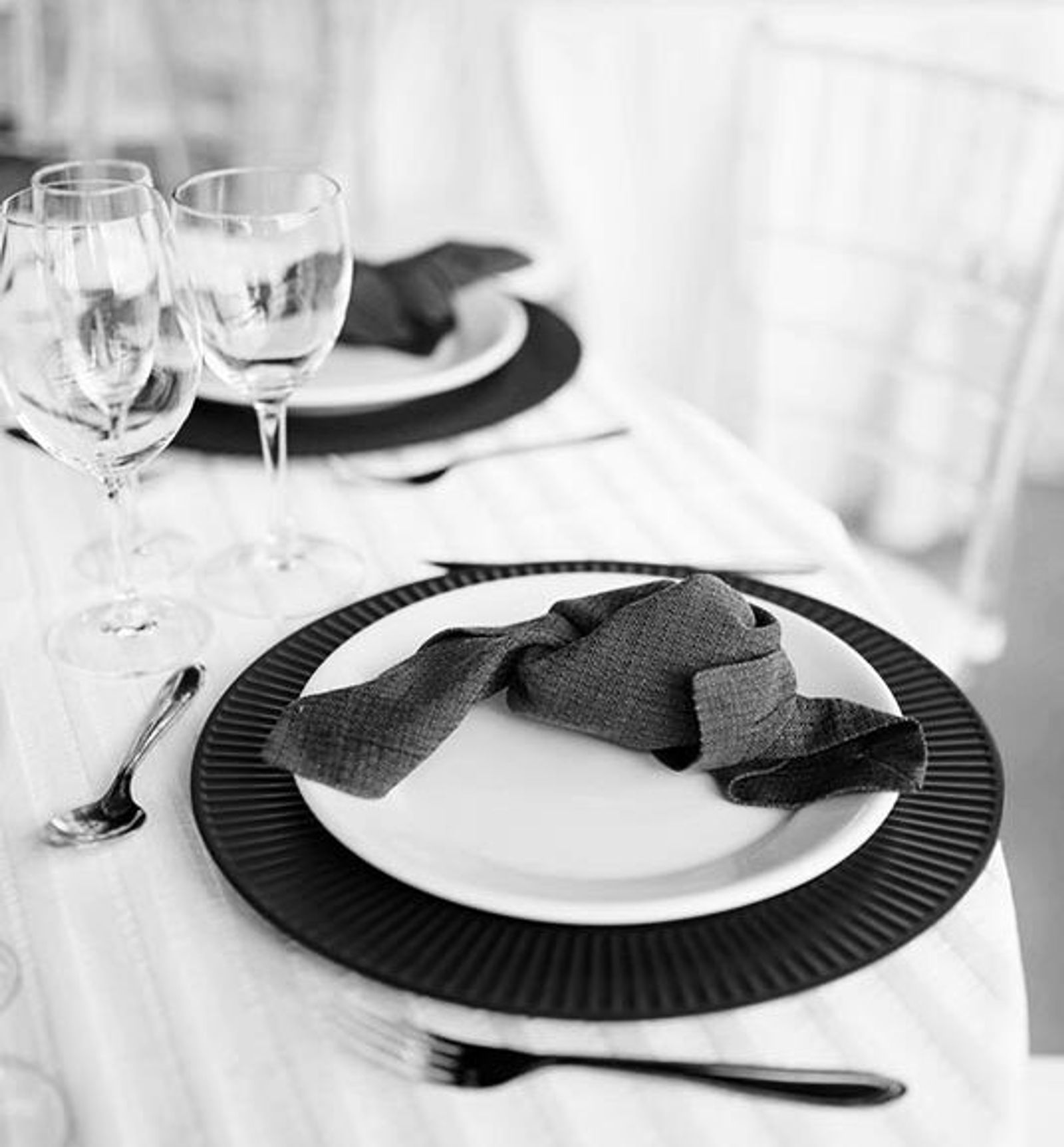 Black-and-white place setting with stacked dark plates, folded napkin, and glassware.