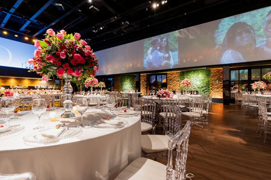 Reception Hall Screen Large reception hall with round tables, a vivid floral centerpiece, and a wide projection screen.
