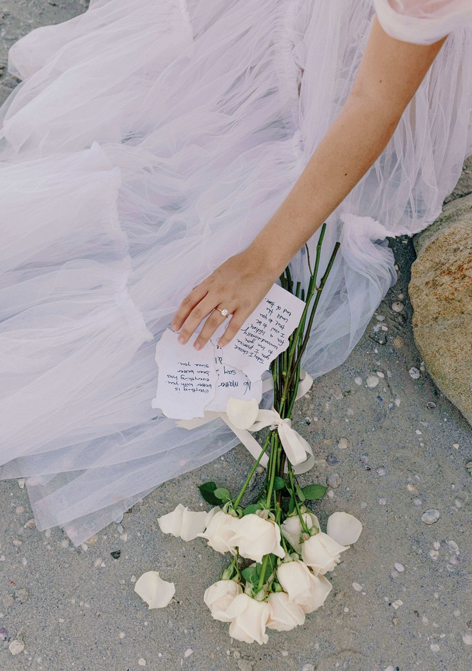 White dress fabric beside a hand holding a paper and a white bouquet