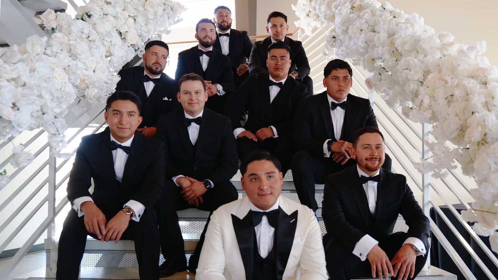 Group of men in formal suits posed on a flower-lined staircase