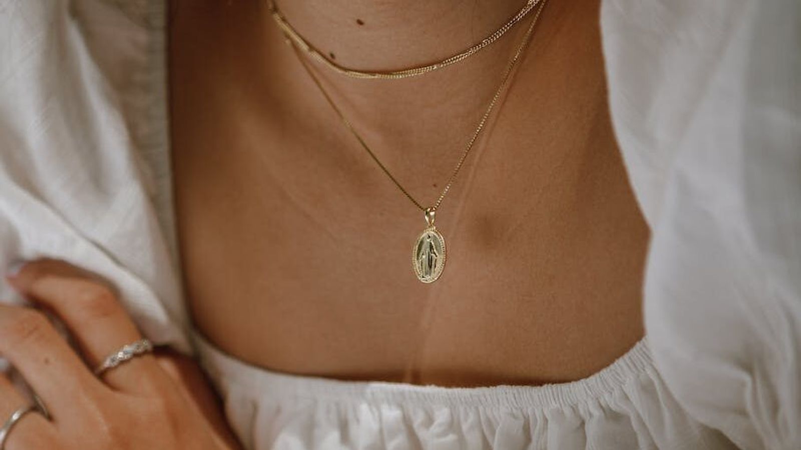 Close-up of layered necklaces and rings above a white garment