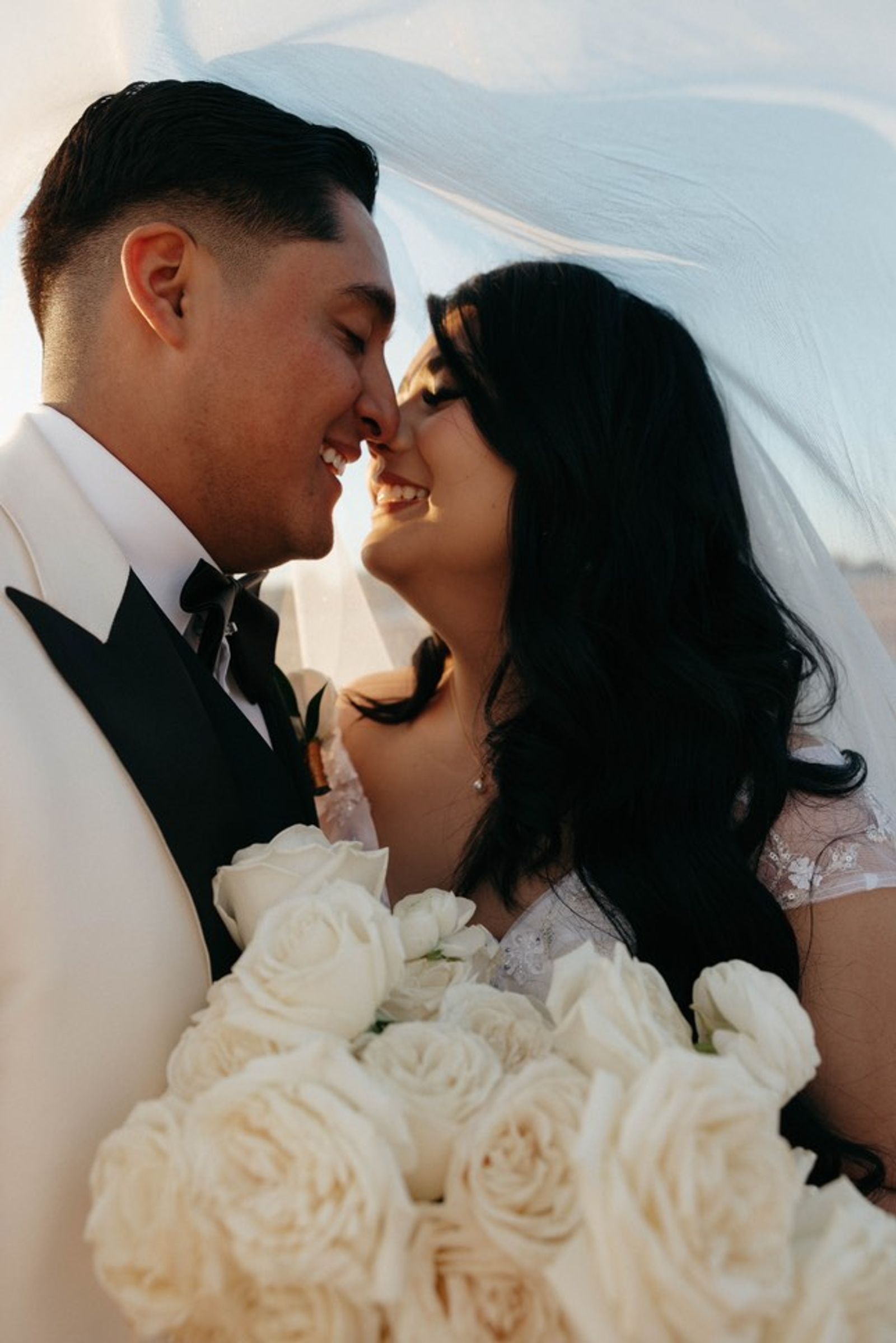 Wedding couple standing close beneath a translucent veil