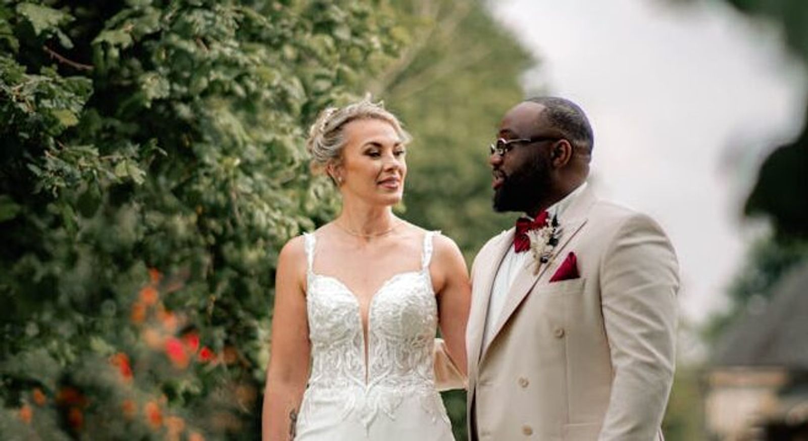 Wedding couple standing outdoors with trees behind them