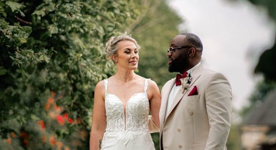 Wedding couple standing outdoors with trees behind them
