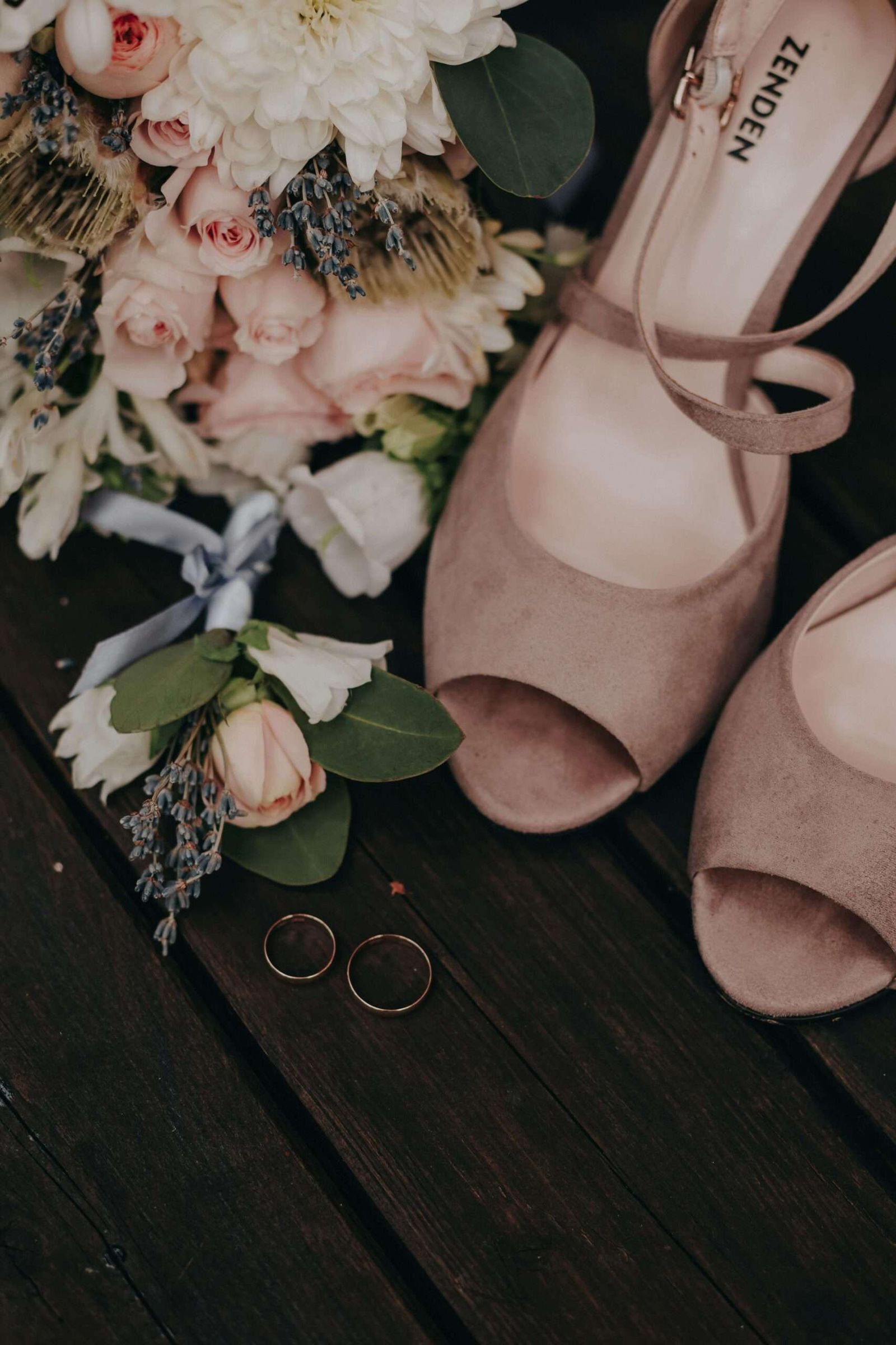 Dark Detail Flat Lay Shoes rings invitation and flowers arranged on a dark wood surface