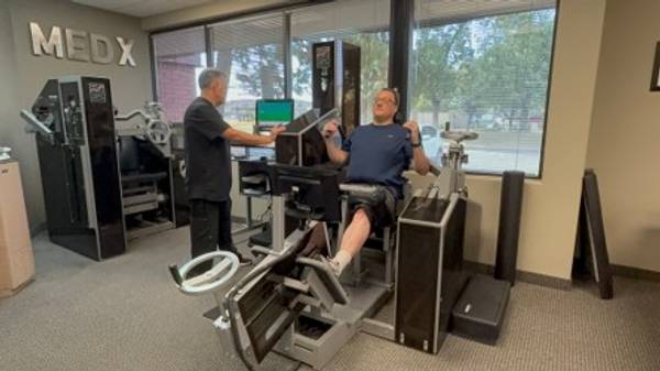 Patient completing supervised, stabilized MedX spinal testing while Armando monitors the equipment at The Center for Total Back Care. 