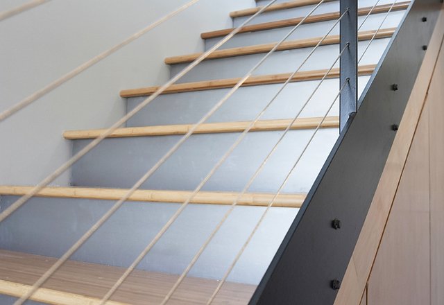 modern staircase with light wood treads gray painted risers and stainless steel cable railing with metal stringer in contemporary home interior