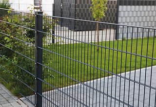 Dark gray powder-coated double wire mesh panel fence installed along green lawn in modern residential garden with paved pathway