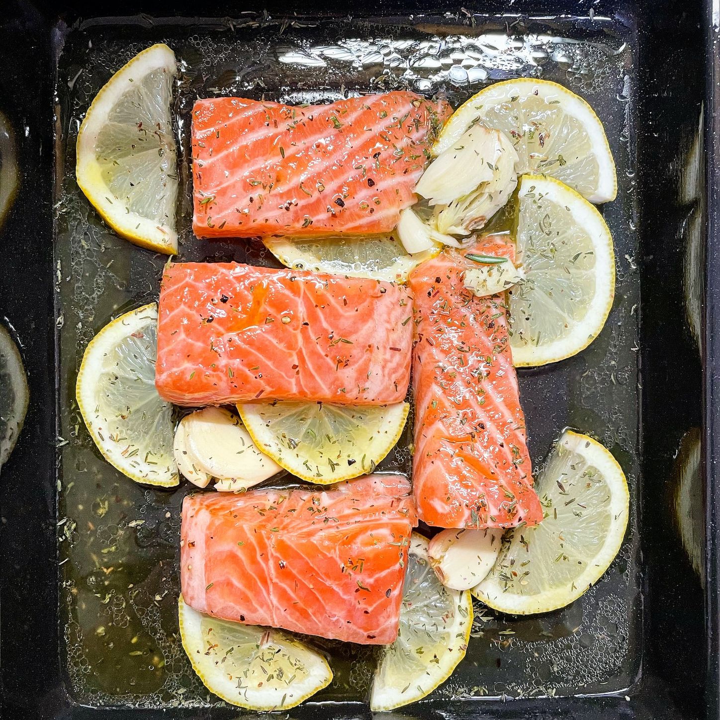 Filets of salmon are spread on a baking sheet with lemon and garlic.