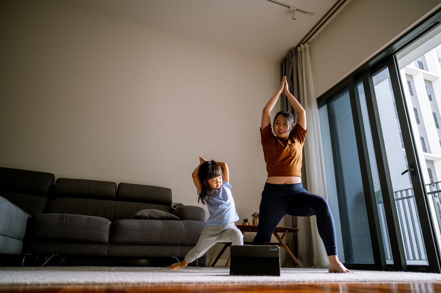 An adult and a toddler practice yoga in their living room.