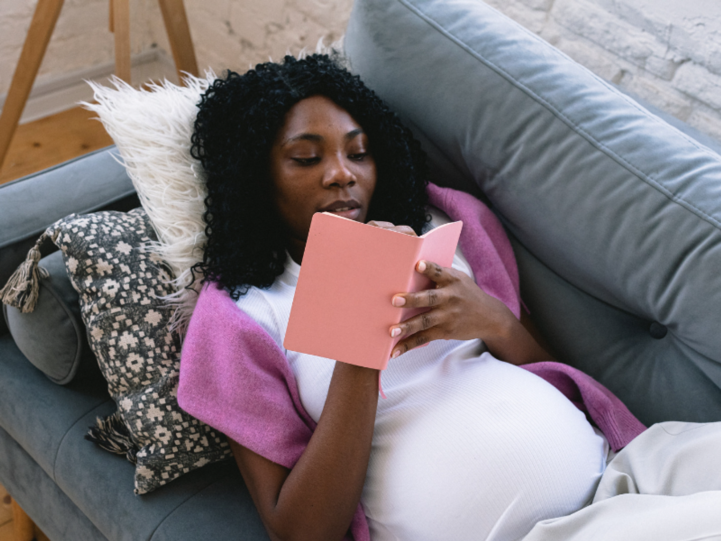 A postpartum mom lies on a couch and writes in her journal.