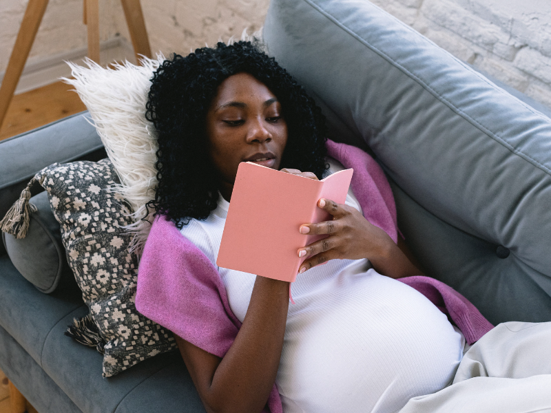 A postpartum mom lies on a couch and writes in her journal.