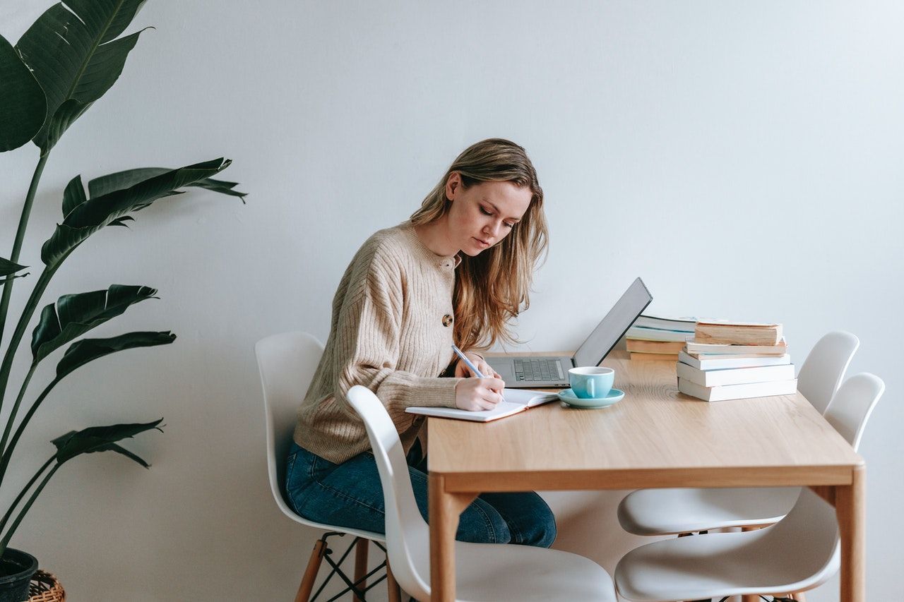 A person sits at a table with a computer and writes notes.