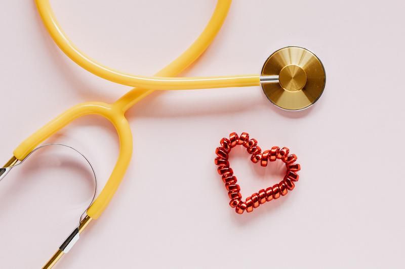 A yellow stethoscope next to a shiny red heart shape.