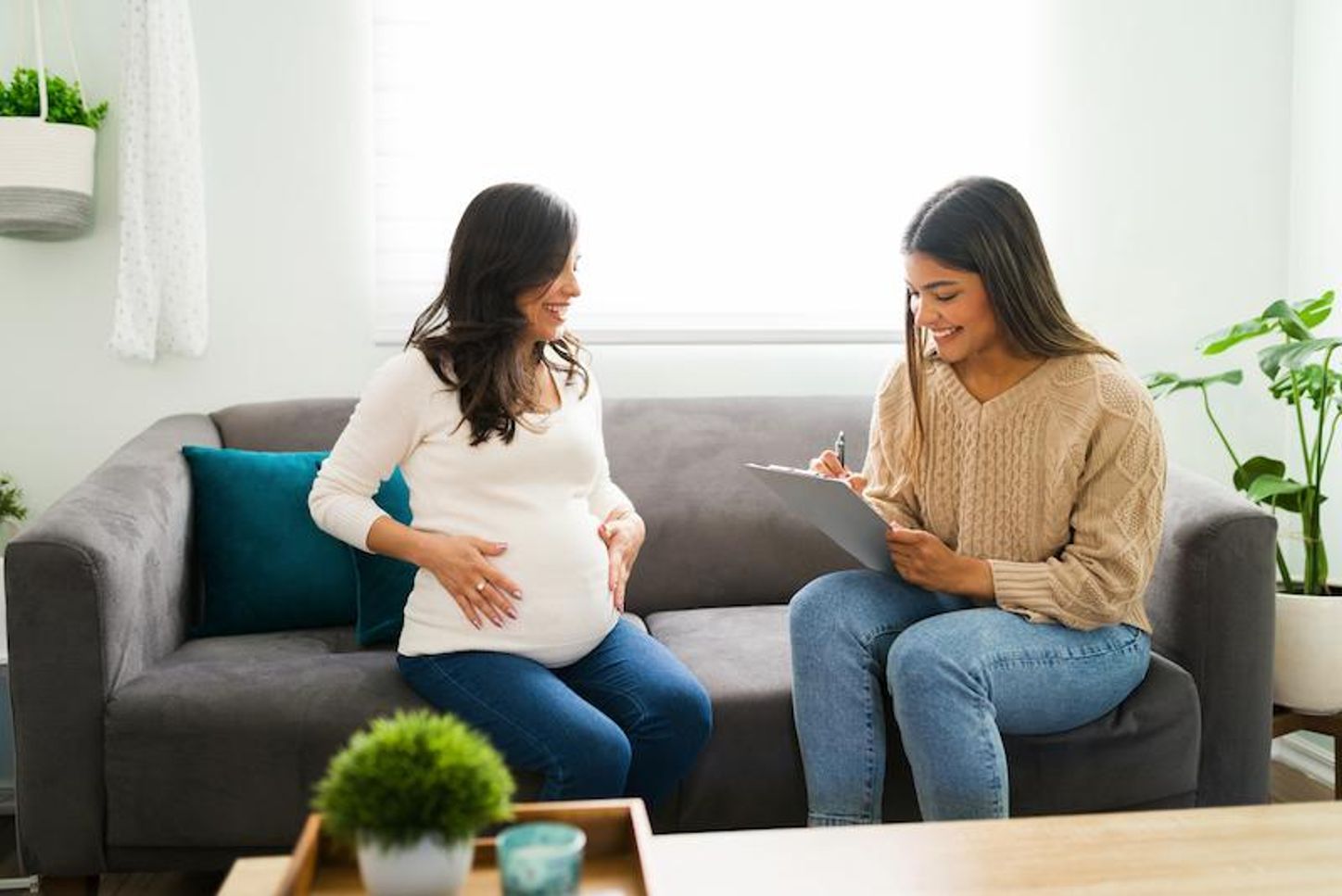 A doula writes information beside her pregnant client on a couch.