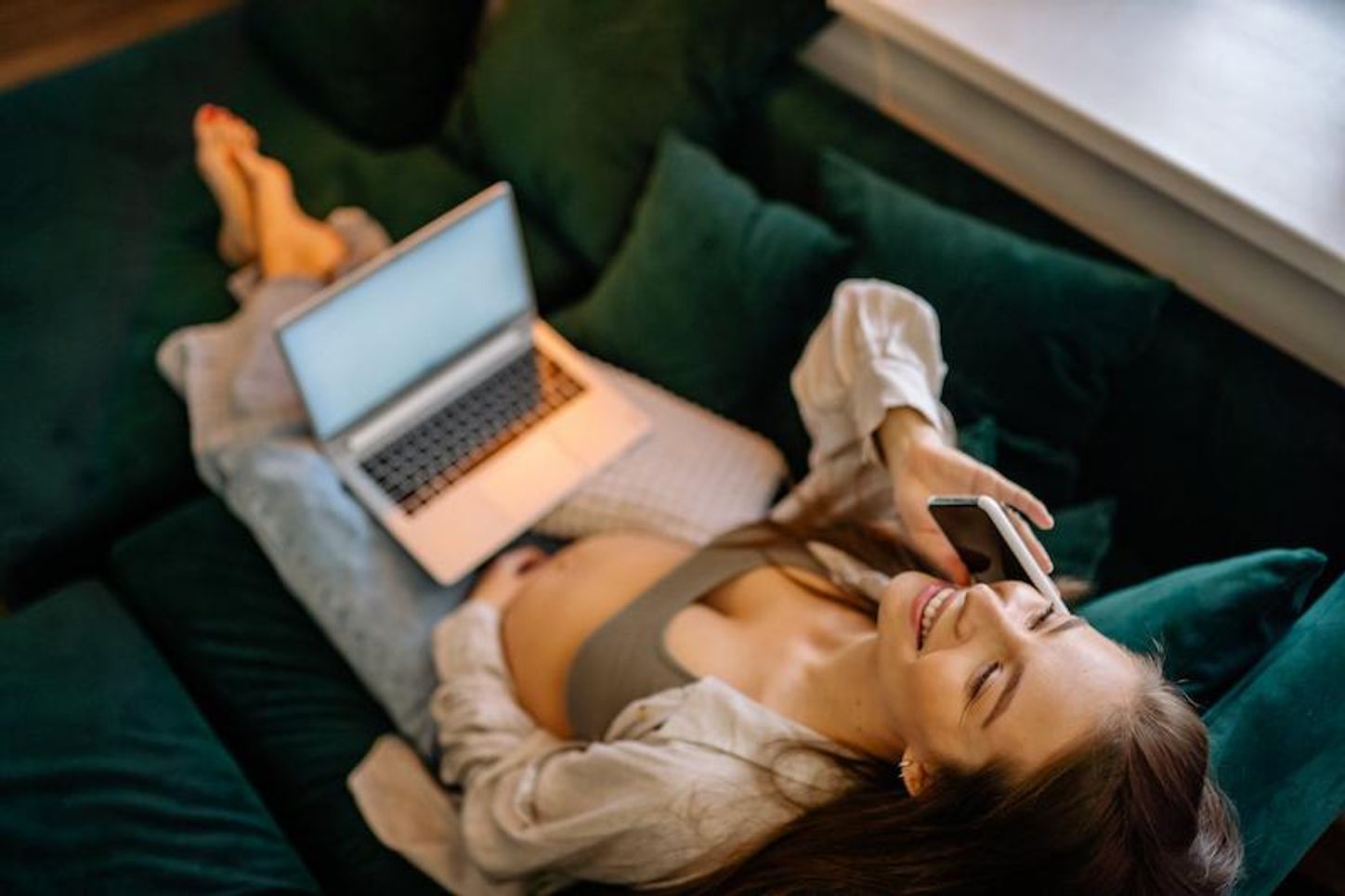 Pregnant person reclining on their couch. They are smiling as they talk on the phone.