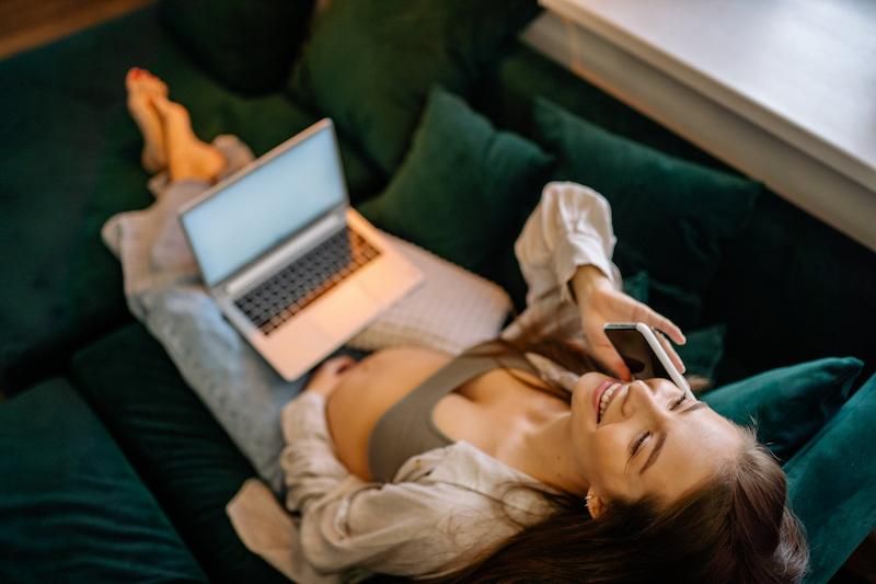 Pregnant person reclining on their couch. They are smiling as they talk on the phone.