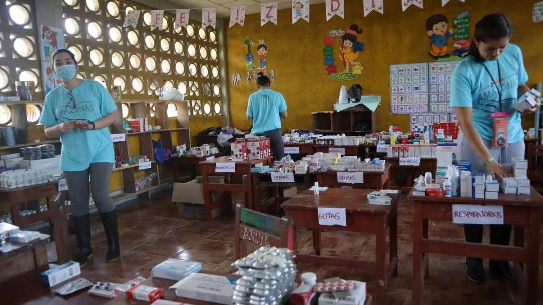 Voluntarios con camisetas turquesa atienden una farmacia improvisada en un aula