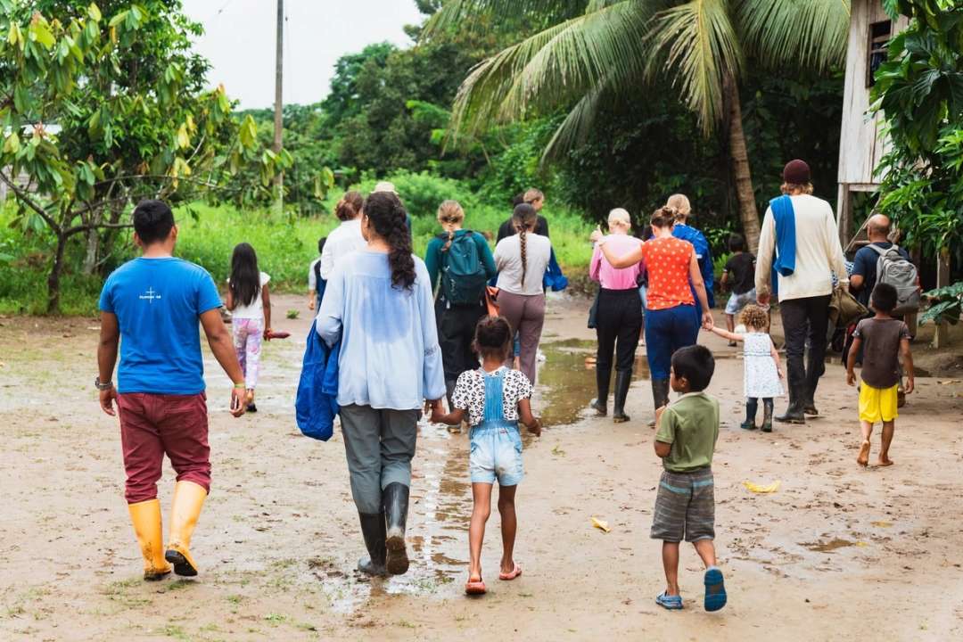 Un grupo de visitantes y niños camina por un sendero de tierra hacia la comunidad
