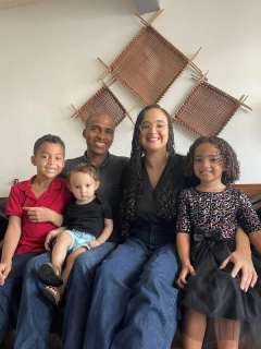 La familia De la Cruz sonríe sentada en un sofá: papá, mamá y tres niños