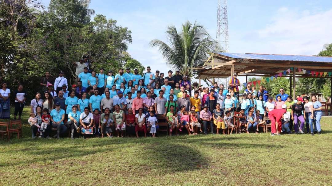 Gran grupo de líderes y familias con camisetas celestes posando bajo las palmeras de una comunidad