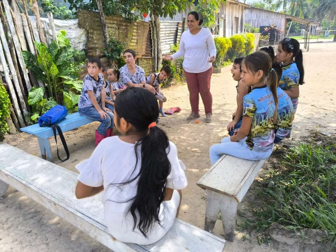 Niños sentados en bancas escuchan a una mujer en una calle de la comunidad
