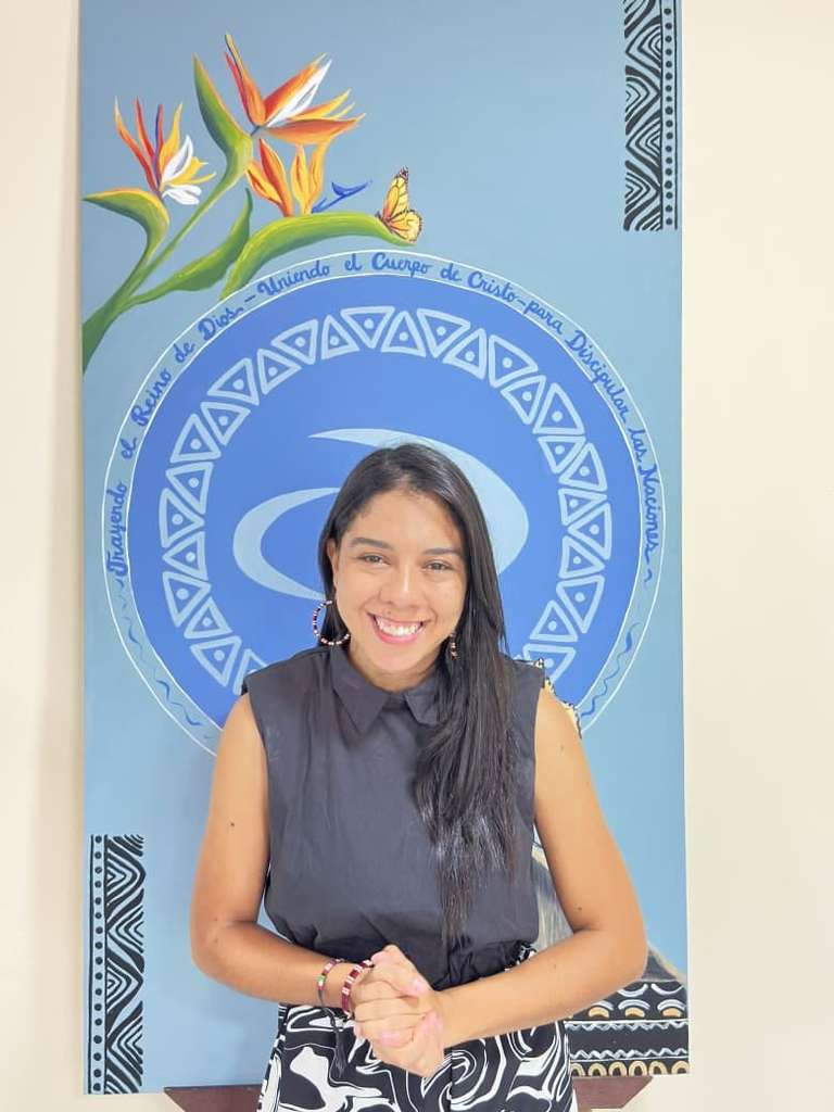 Natalia Hincapié sonriendo frente a un mural azul con el emblema de JUCUM