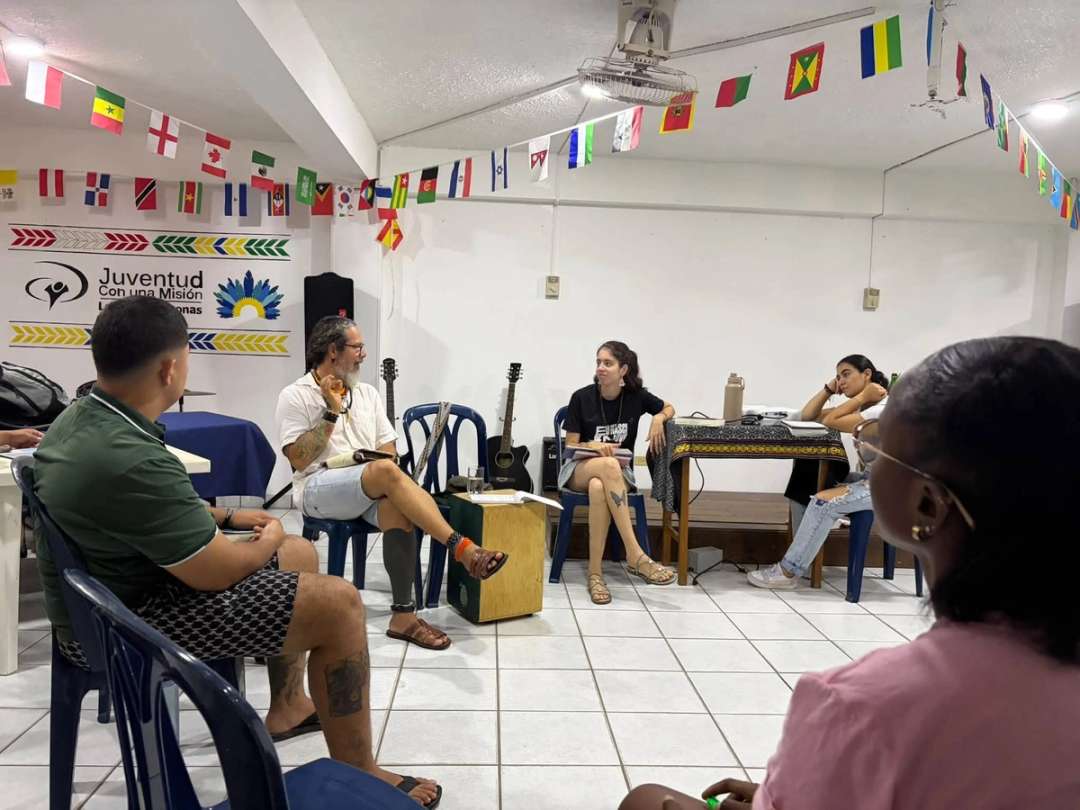 Estudiantes sentados en círculo con guitarras bajo banderas de muchas naciones