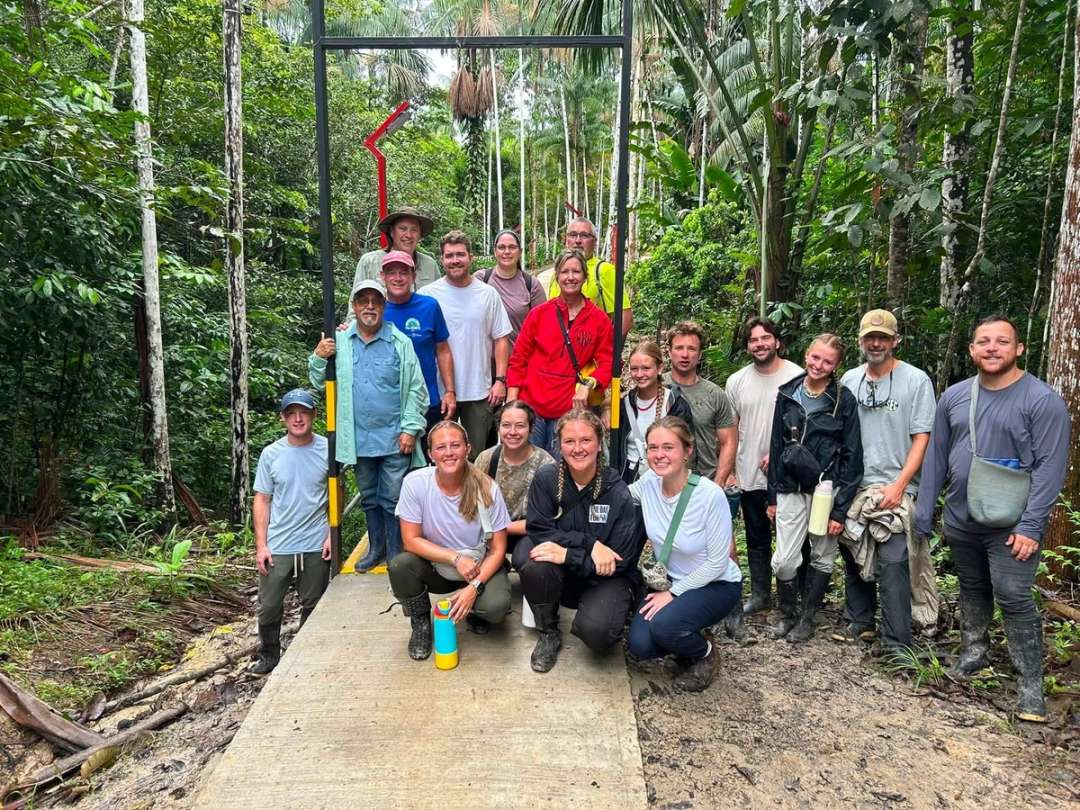 Equipo de voluntarios posa en una pasarela de concreto entre palmas y selva