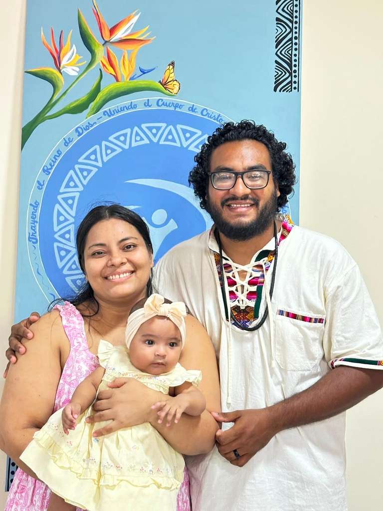 La familia Escobar, una pareja con su bebé, frente a un mural de la selva