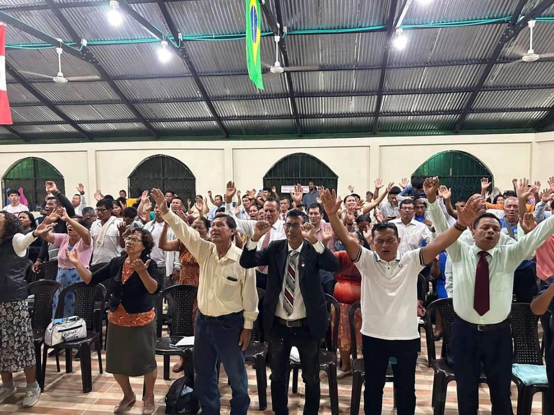 Pastores y líderes con los brazos en alto adoran dentro de un salón