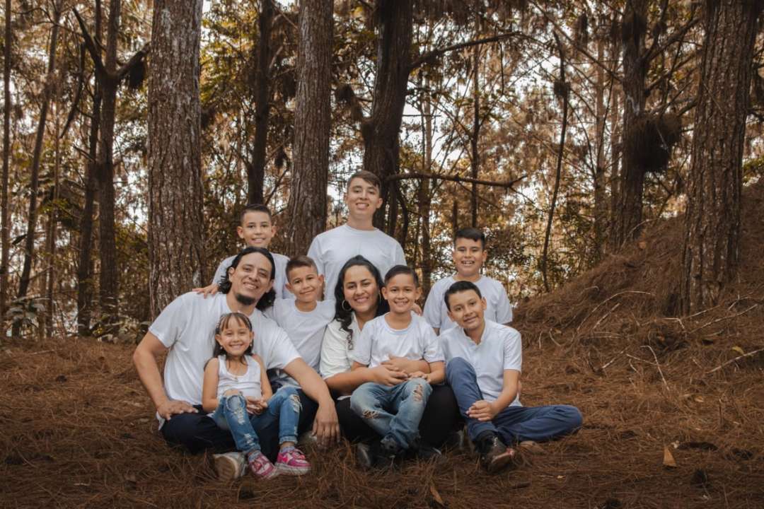 La familia Ayala Sequeda sentada entre pinos, vestida de blanco, con sus hijos