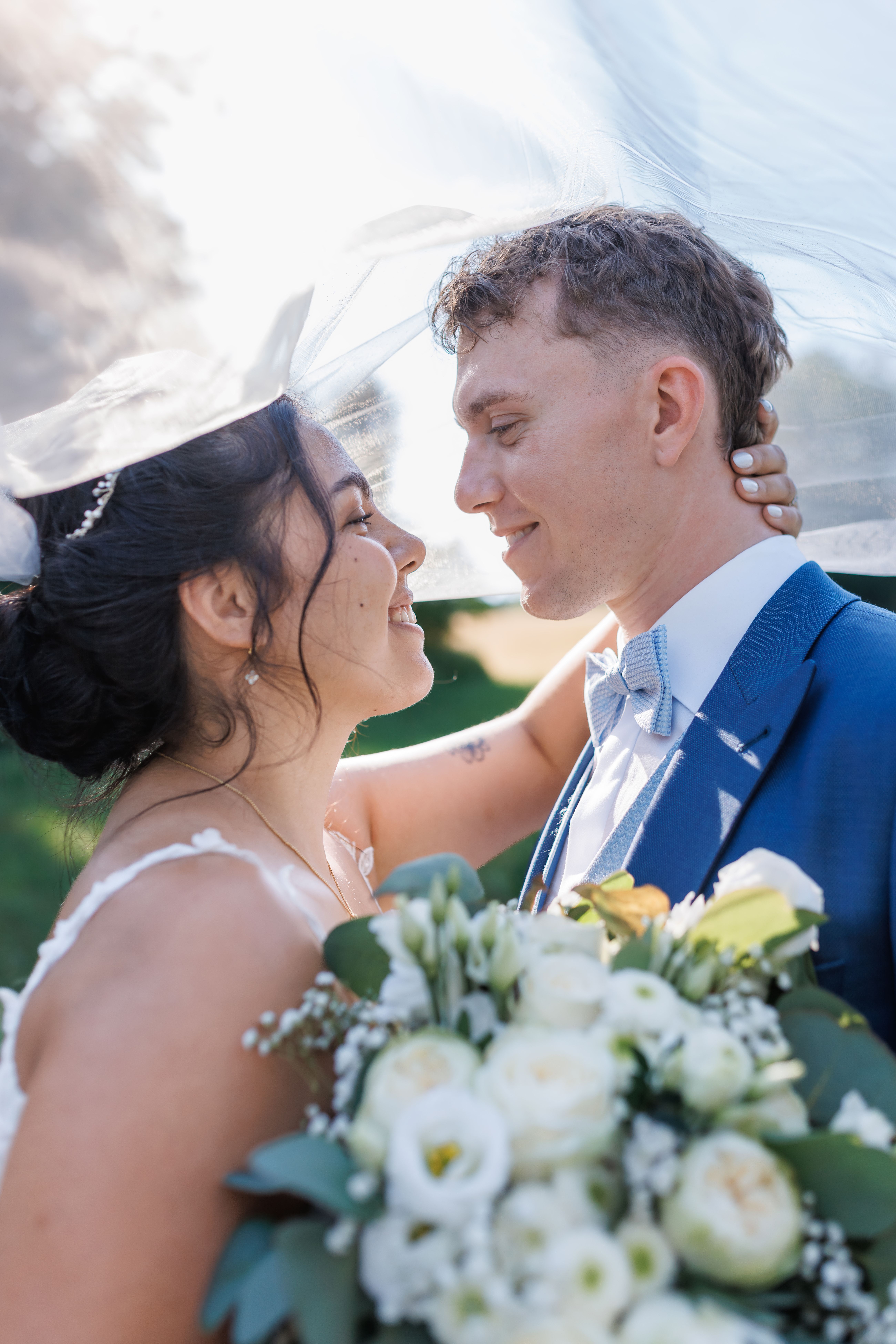 Stefanie und Manuel berühren sich mit den Nasen, der Brautstrauß im Gegenlicht