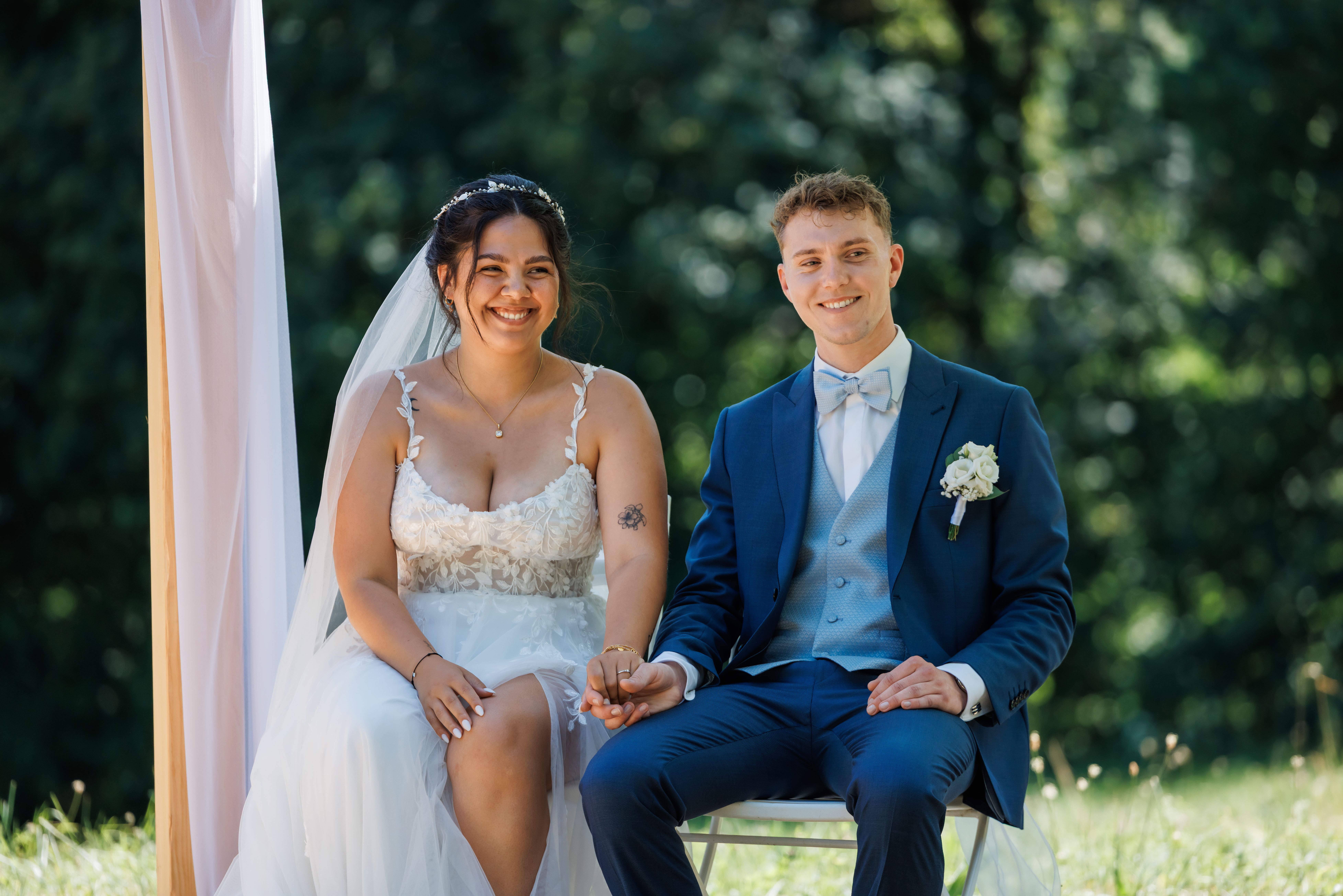 Stefanie und Manuel sitzen Hand in Hand unter dem Trau-Bogen während der freien Trauung
