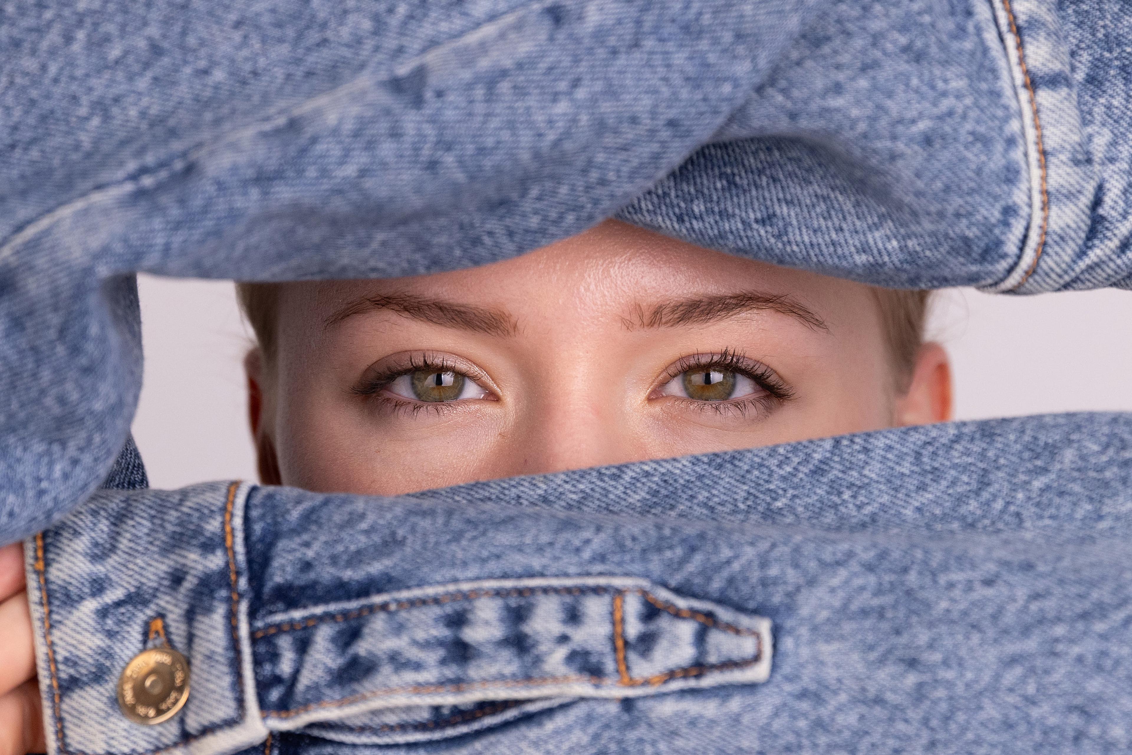 Konzeptportrait: Annette hält eine Jeansjacke vor das Gesicht, nur die Augen blicken über den Stoff.