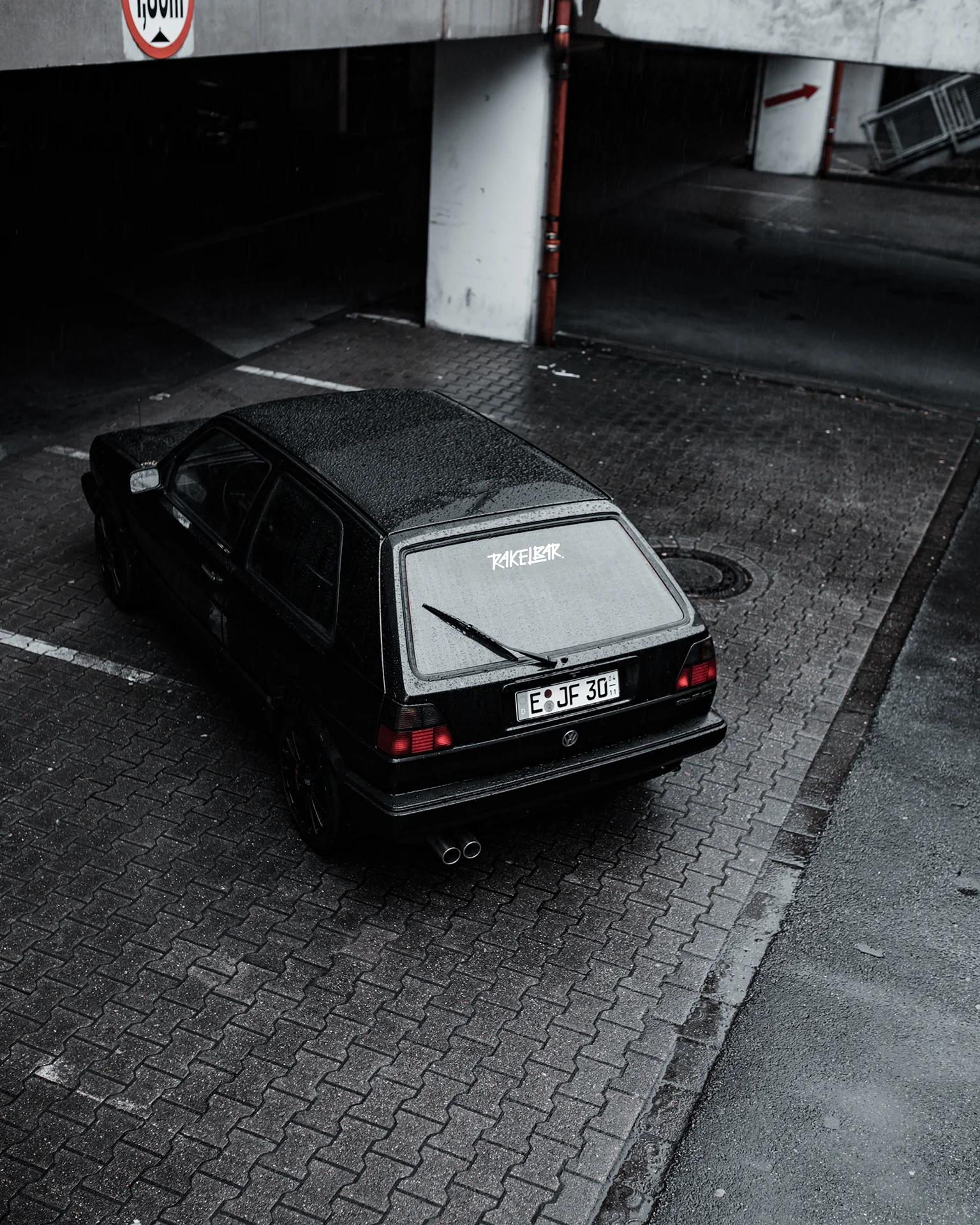 Schwarzer VW Golf II von schräg hinten in einem Parkhaus, mit dem Rakelbar-Schriftzug als Aufkleber auf der Heckscheibe.