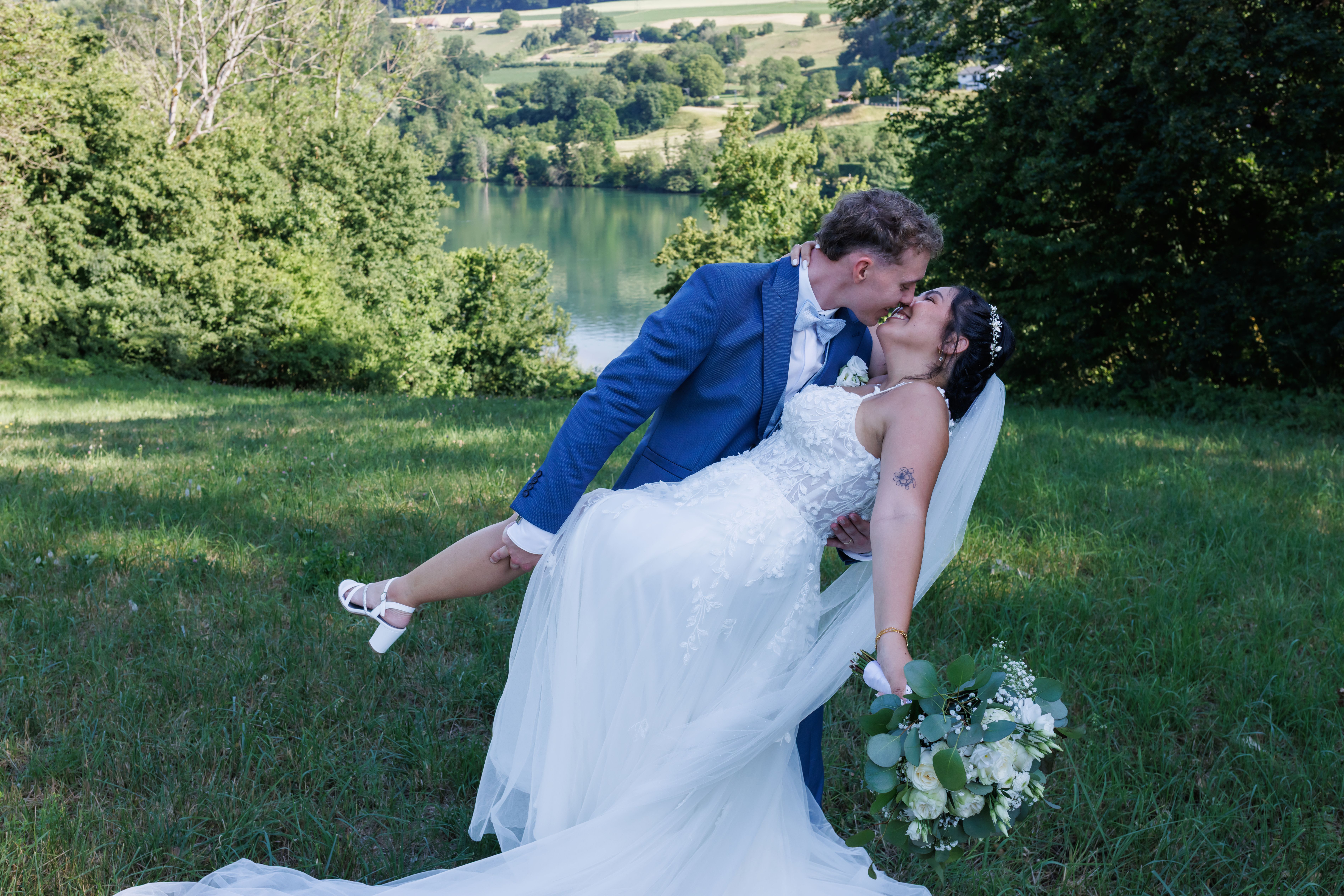 Manuel neigt Stefanie im Dip nach hinten und küsst sie, See und Hügel im Hintergrund