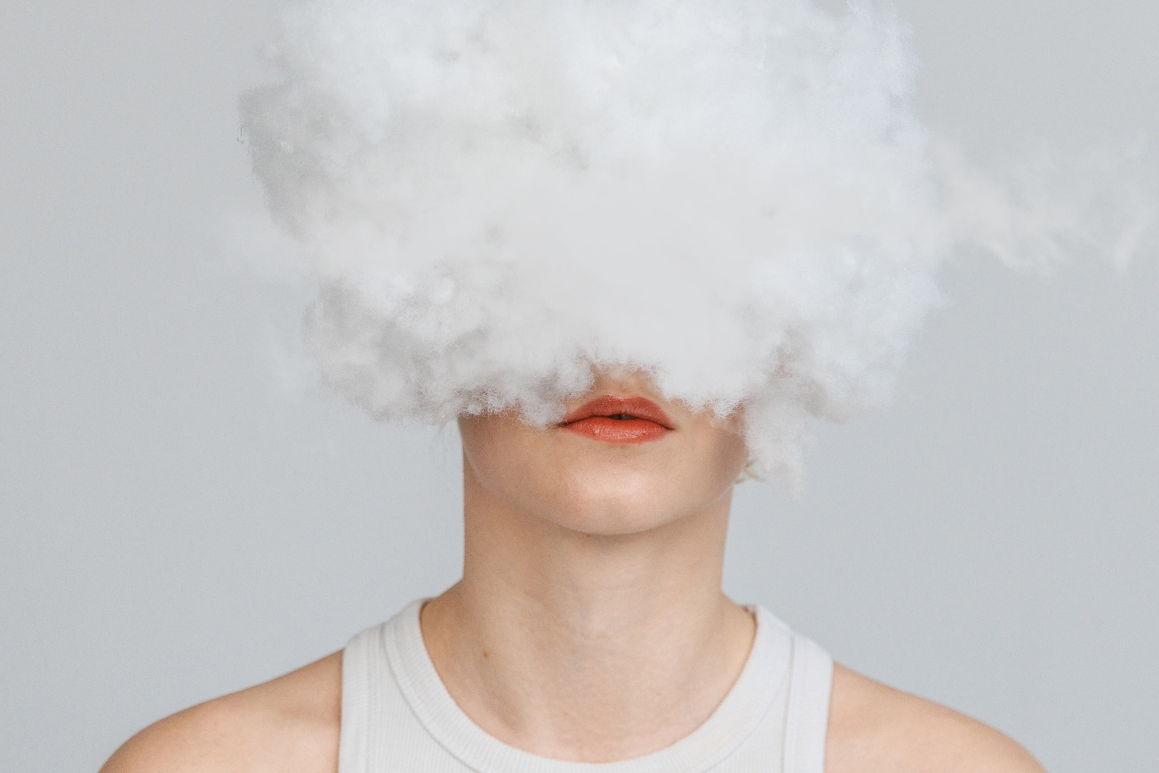 Konzeptportrait von Annette: eine Wolke aus Bastelwatte verdeckt das Gesicht, nur der Mund bleibt sichtbar, heller Studiohintergrund.