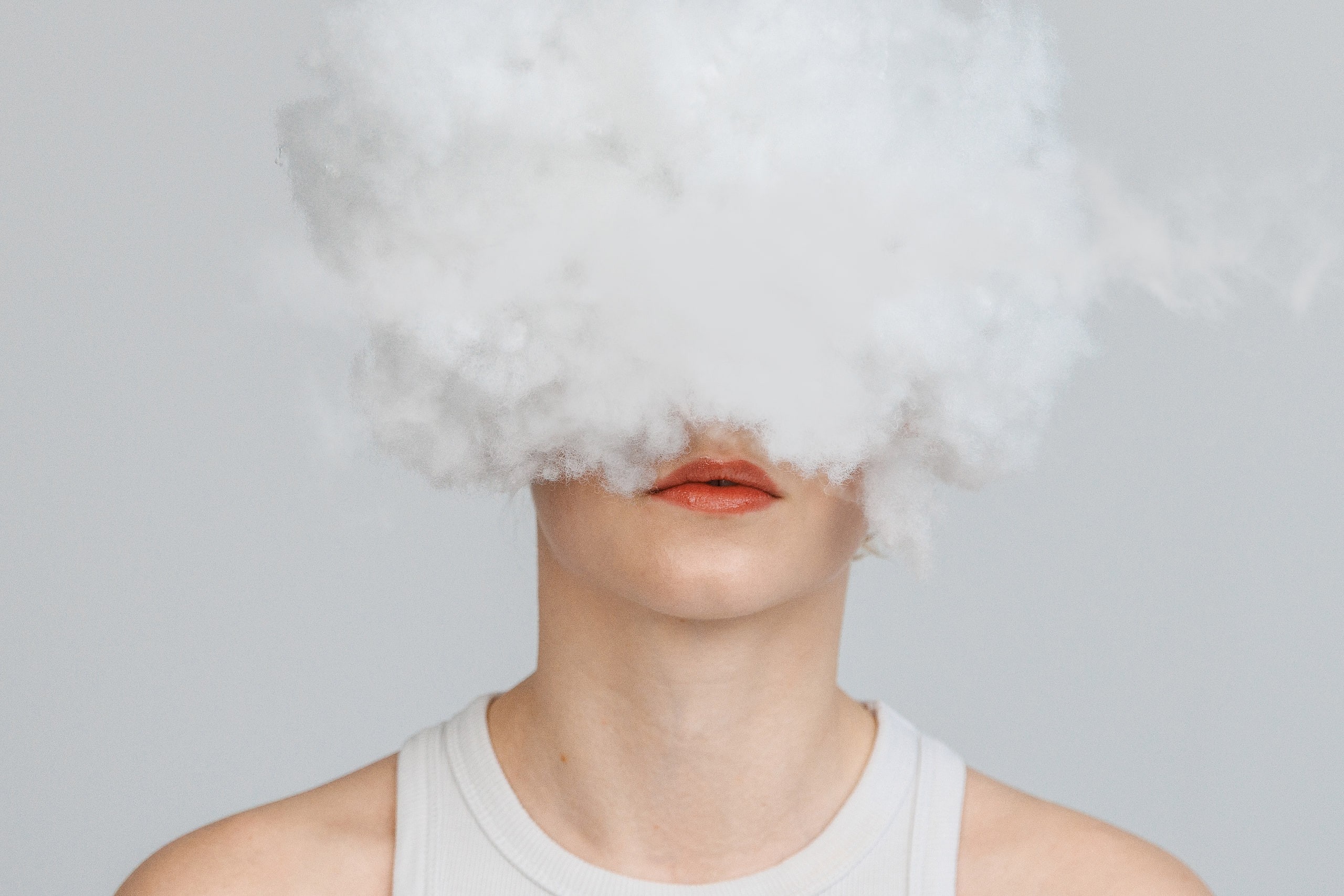Konzeptportrait von Annette: eine Wolke aus Bastelwatte verdeckt das Gesicht, nur der Mund bleibt sichtbar, heller Studiohintergrund.