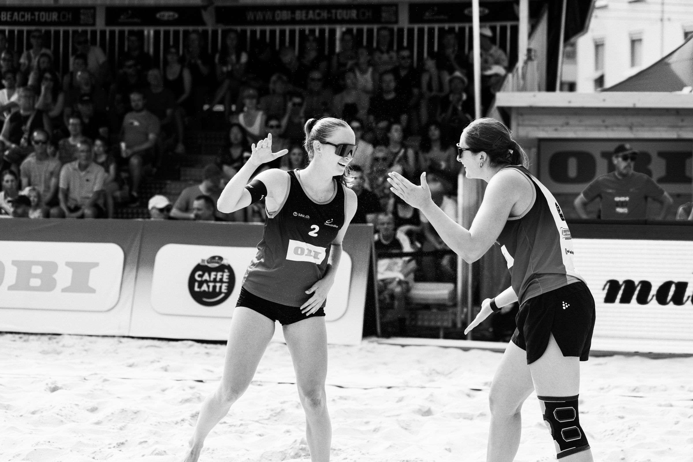 Jasmine Wandeler und Livia Stolz klatschen sich ab, Schwarzweißaufnahme, im Spiel Wandeler/Stolz gegen Eugster/Gähwiler bei der OBI Beach Tour 2026 in Basel.