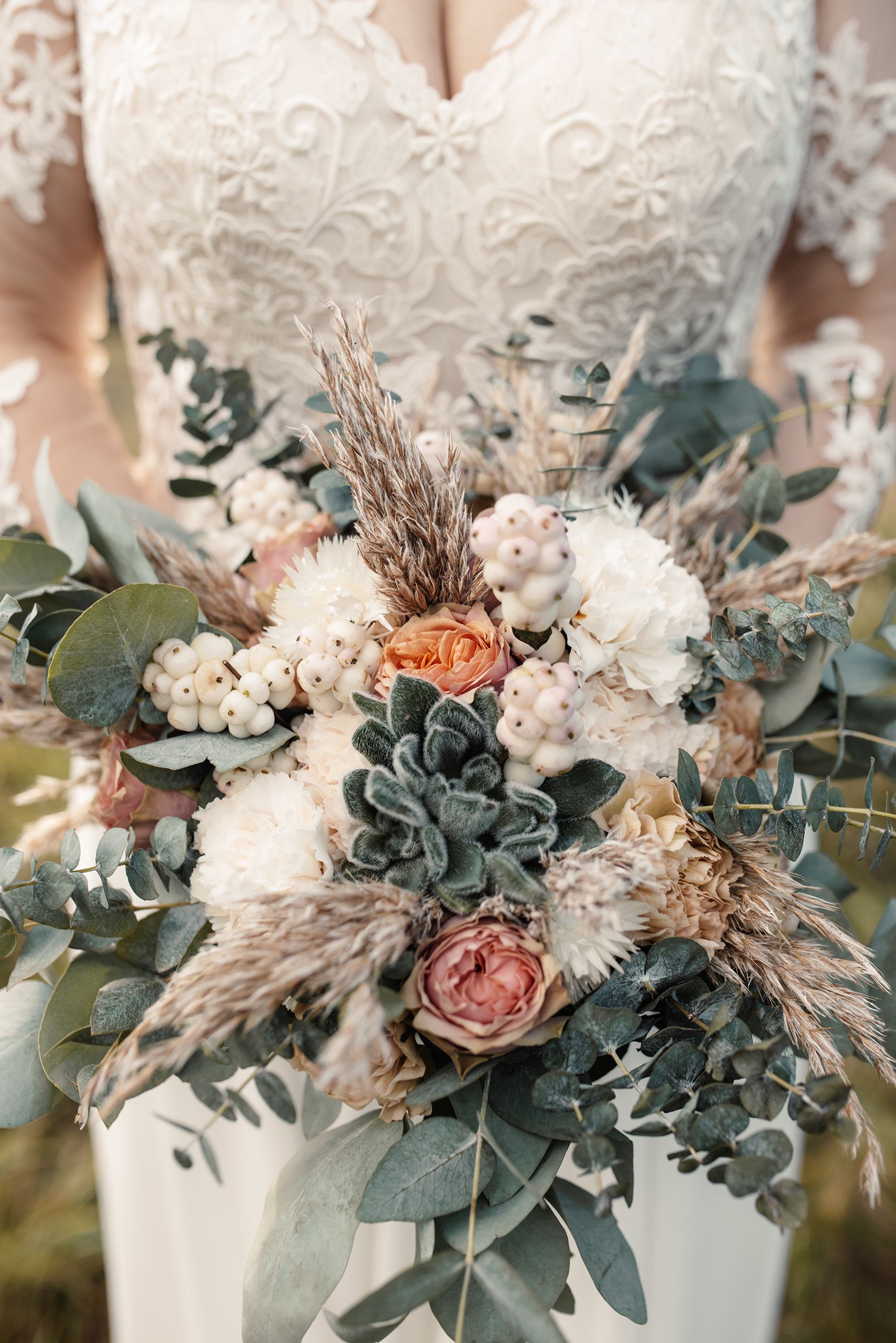 Brautstrauß aus Trockenblumen, Eukalyptus und Rosen vor dem Spitzenkleid