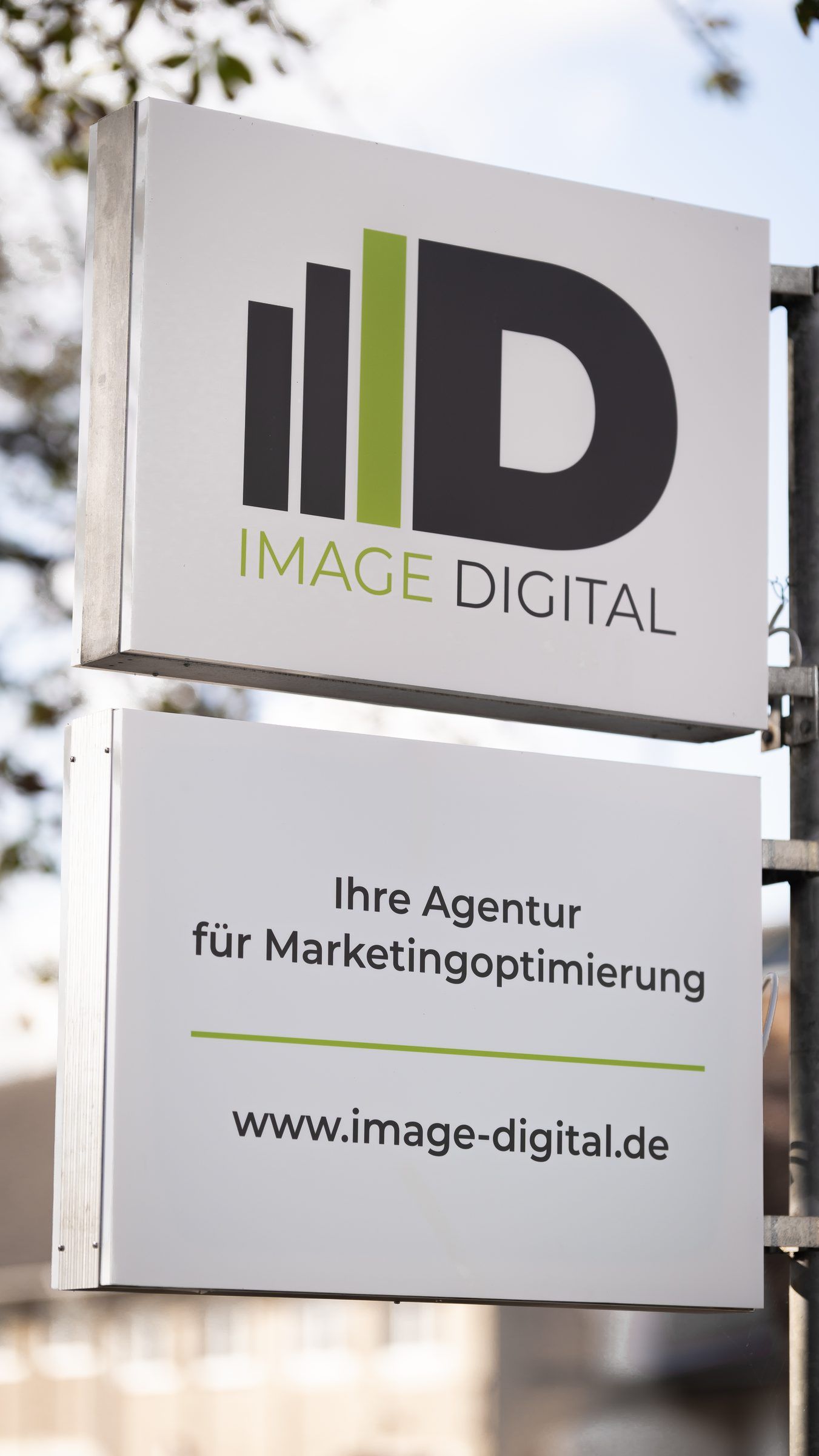 Außen-Werbeschild von Image Digital mit dem Zusatz Ihre Agentur für Marketingoptimierung, dahinter die Fahnen.